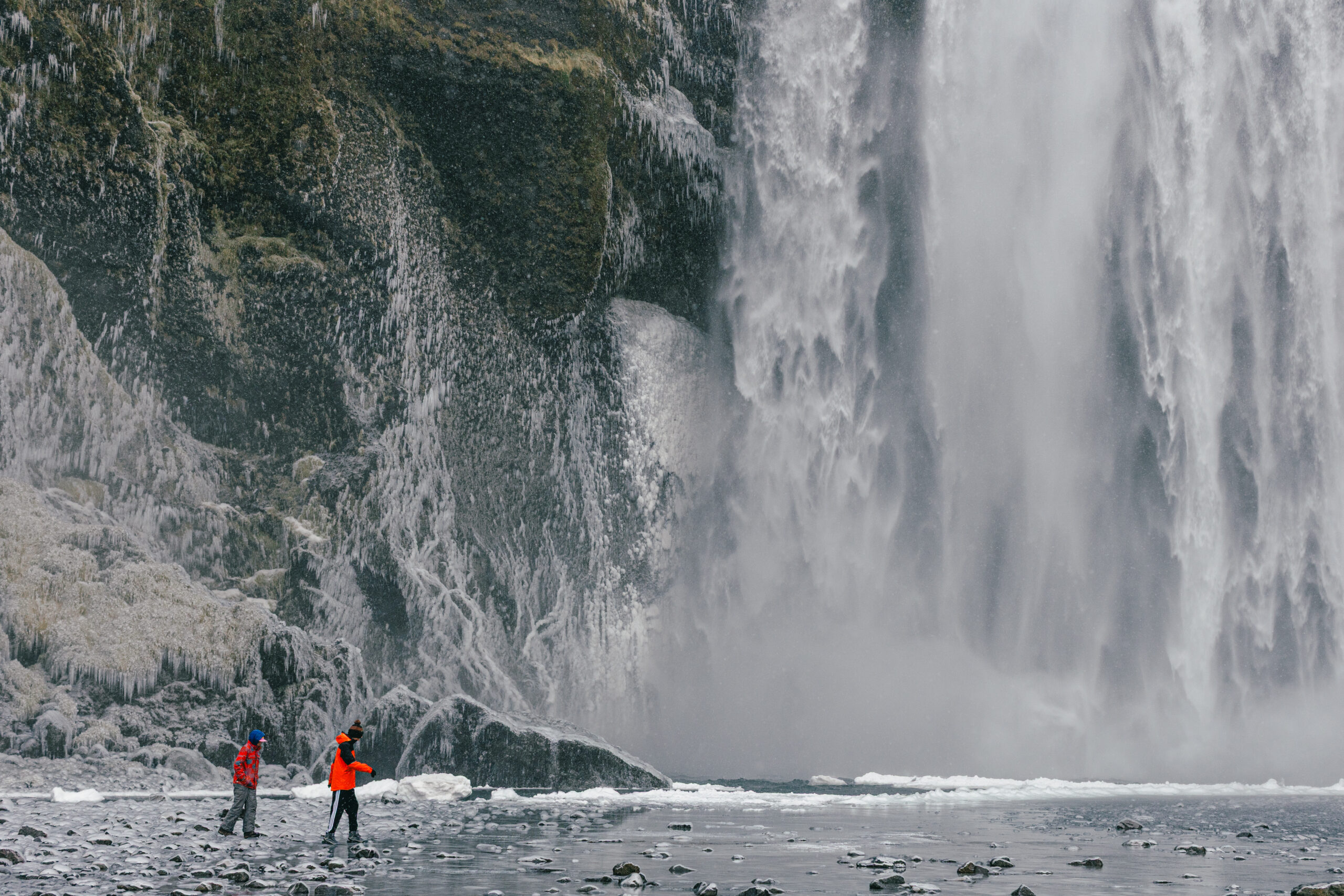 two boys in bright coats stand in front of a waterfall in Iceland